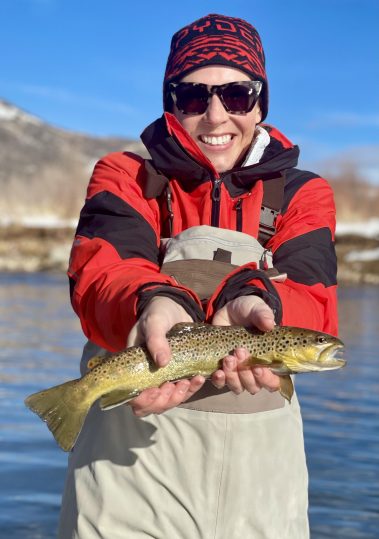 A woman with a brown trout caught while fly fishing in the Winter