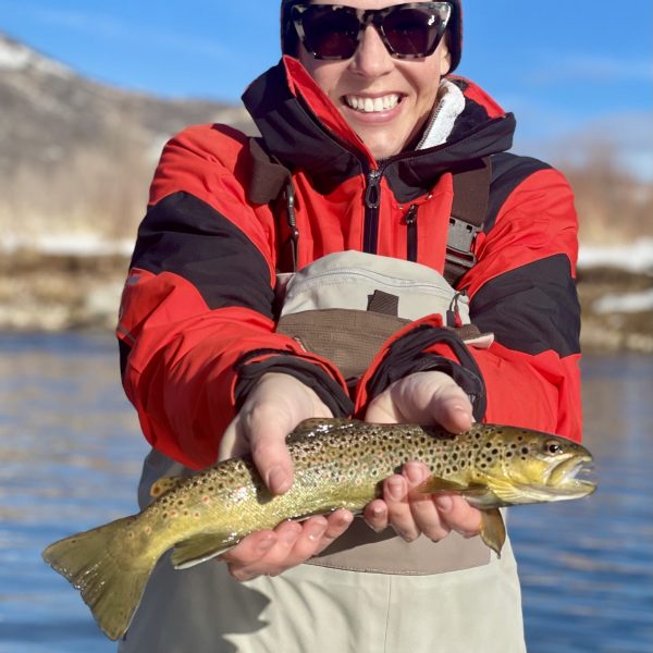 A woman with a brown trout caught while fly fishing in the Winter