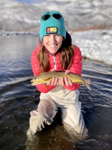 A woman with a brown trout caught while fly fishing in the Winter
