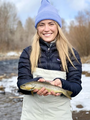 A woman with a brown trout caught while fly fishing in the Winter