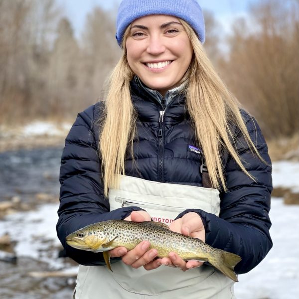 A woman with a brown trout caught while fly fishing in the Winter