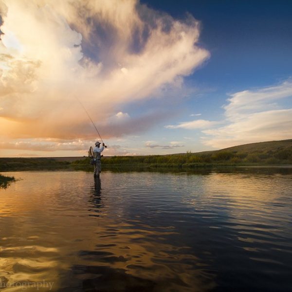 A fly fisherman casting to a rising trout with a beautiful sunset.