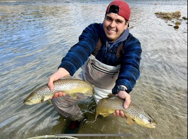 A fly fisherman holding two brown trout he caught at the same time in a small stream in Utah.