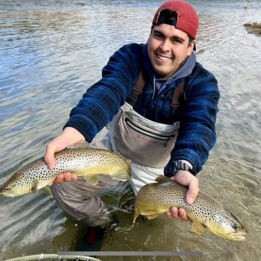 A fly fisherman holding two brown trout he caught at the same time in a small stream in Utah.
