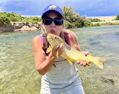 A happy fly fisherwoman about to kiss a big brown trout she caught in Utah