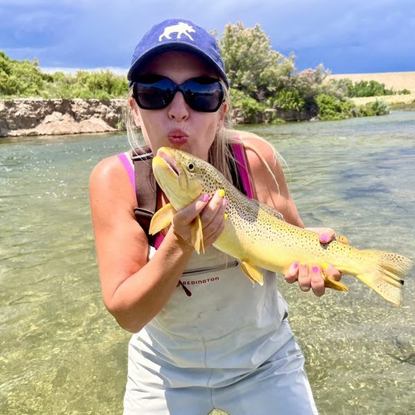 A happy fly fisherwoman about to kiss a big brown trout she caught in Utah