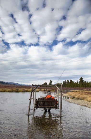 A fly fisherman sitting on a swing in the Madison River