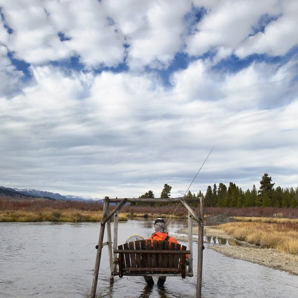 A fly fisherman sitting on a swing in the Madison River