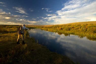 A fly fisherman standing in a western river with a sunset in the back ground