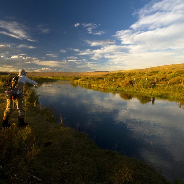 A fly fisherman standing in a western river with a sunset in the back ground