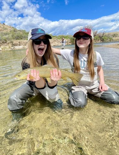 Fly fishing sisters with a big brown trout caught on a Utah river.