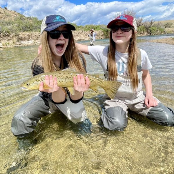 Fly fishing sisters with a big brown trout caught on a Utah river.