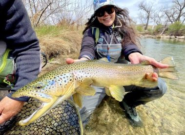 A lady holding a large brown trout. She is the current big fish leader for 2025