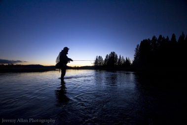 Fly fisherman standing in a Montana River at dusk