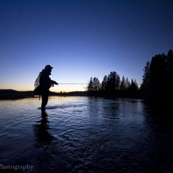 Fly fisherman standing in a Montana River at dusk