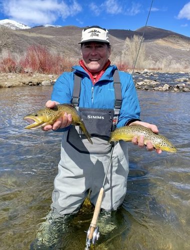 Fly fisherman standing in the Provo River holding two brown trout caught on a guided fly fishing trip.