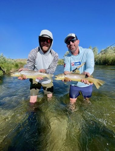 Two fly fisherman standing in a Utah stream holding big brown trout