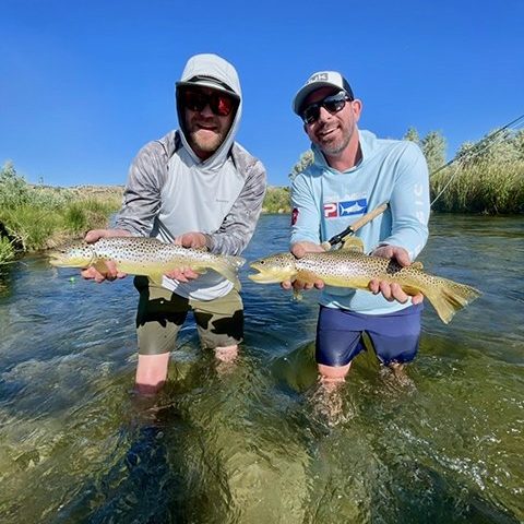 Two fly fisherman standing in a Utah stream holding big brown trout