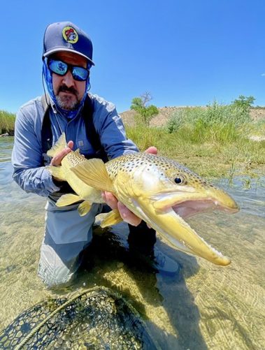 A fly fisherman holding a big brown trout caught with fly fishing guide Jeremy Allan